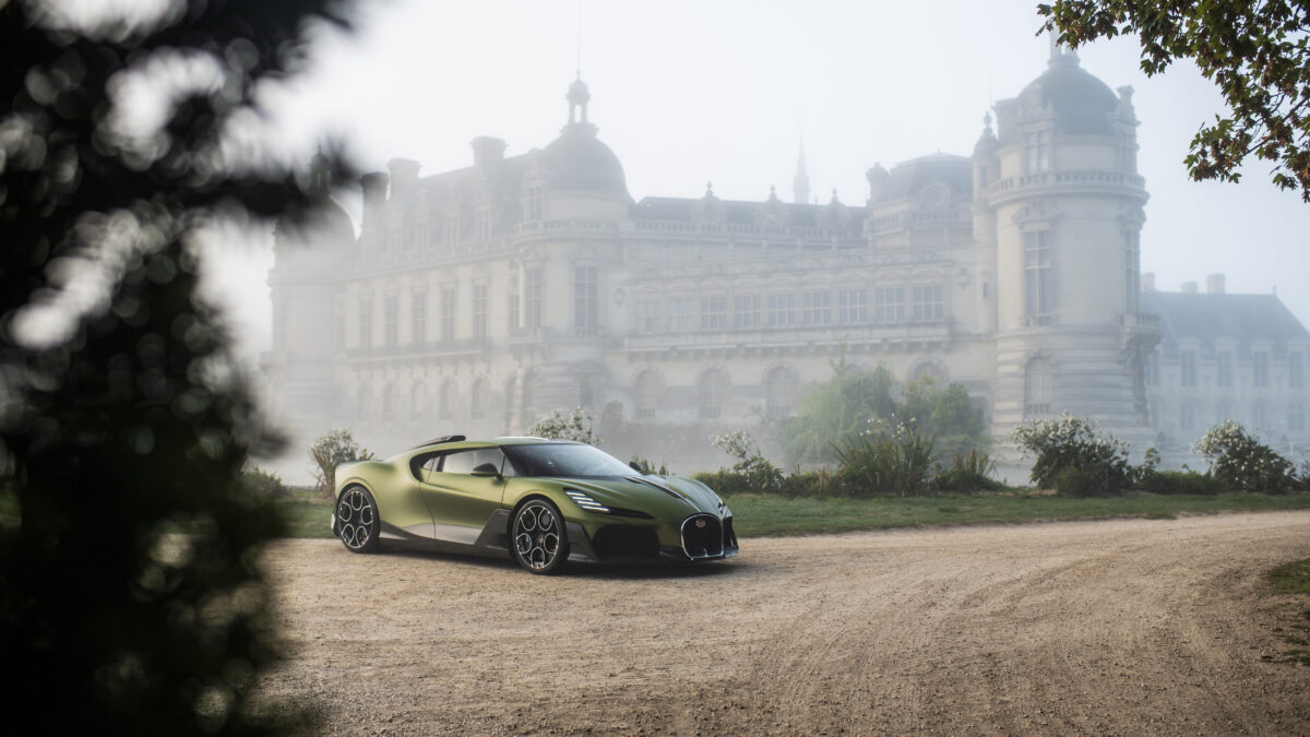 A green Bugatti sports car parked on a gravel drive in front of the fog-shrouded Château de Chantilly.
