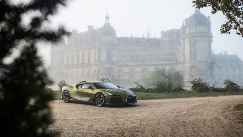 A green Bugatti sports car parked on a gravel drive in front of the fog-shrouded Château de Chantilly.