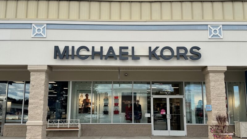 Exterior of a Michael Kors retail store with signage and display windows in a shopping plaza.
