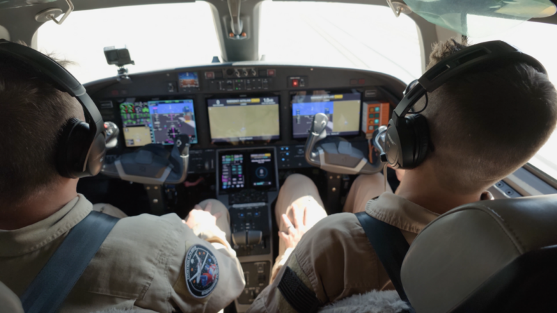 Two pilots in a Cessna Citation CJ4 Gen3 cockpit with an Emergency Autoland message displayed on the avionics screen.