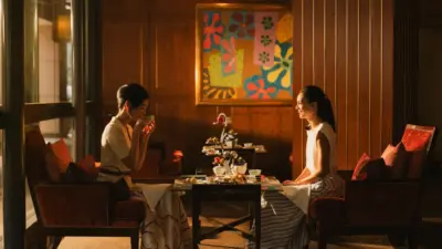 Two women sit at a table having afternoon tea in an elegant hotel lounge with warm lighting.