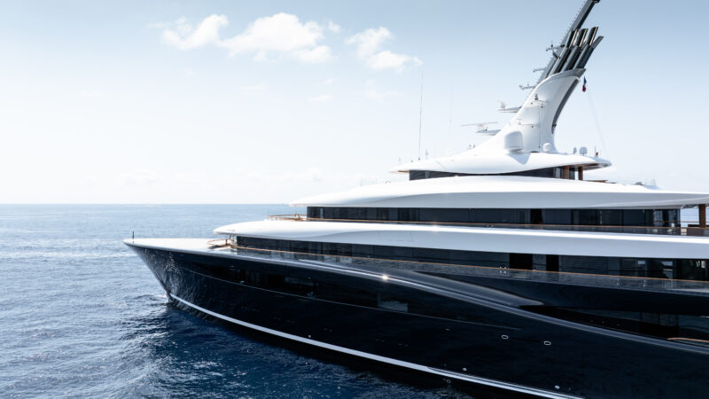 Bow and upper decks of a large black-hulled superyacht photographed at sea under a partly cloudy sky.