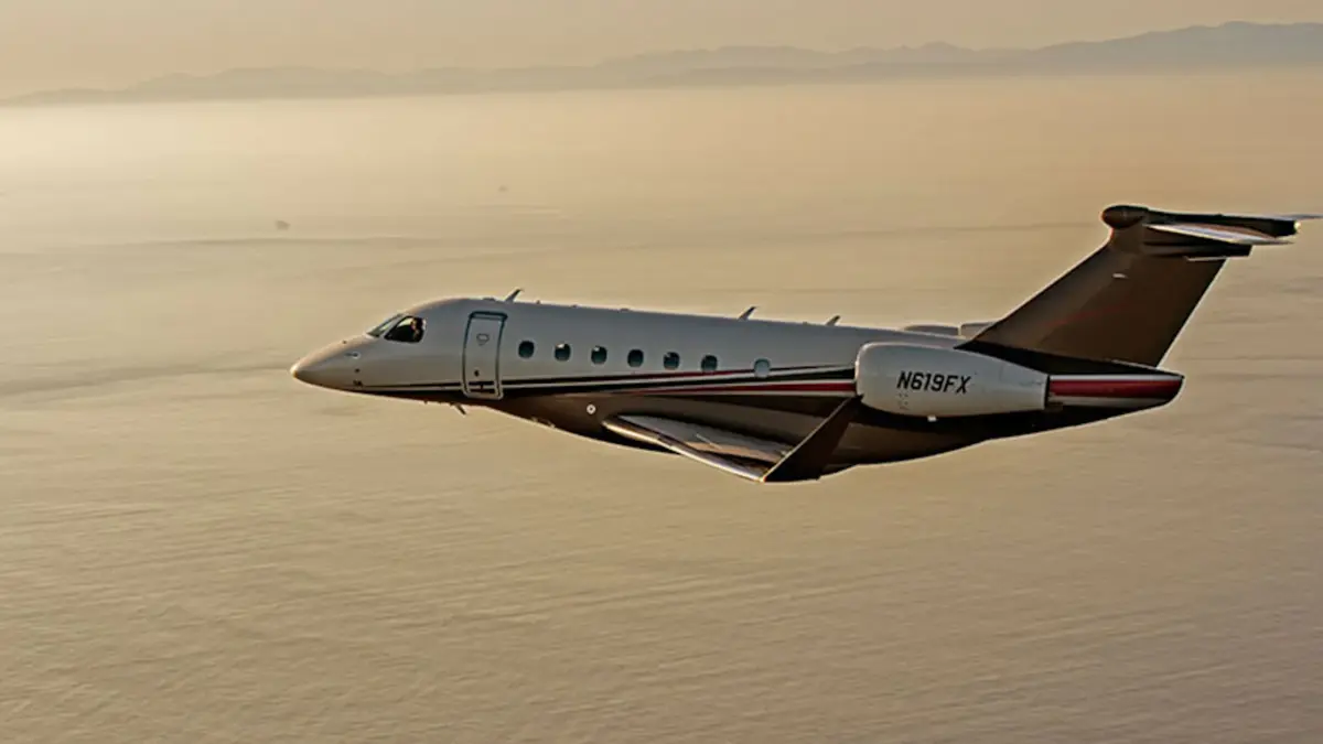 A private jet with registration N619FX flying over water at sunset.
