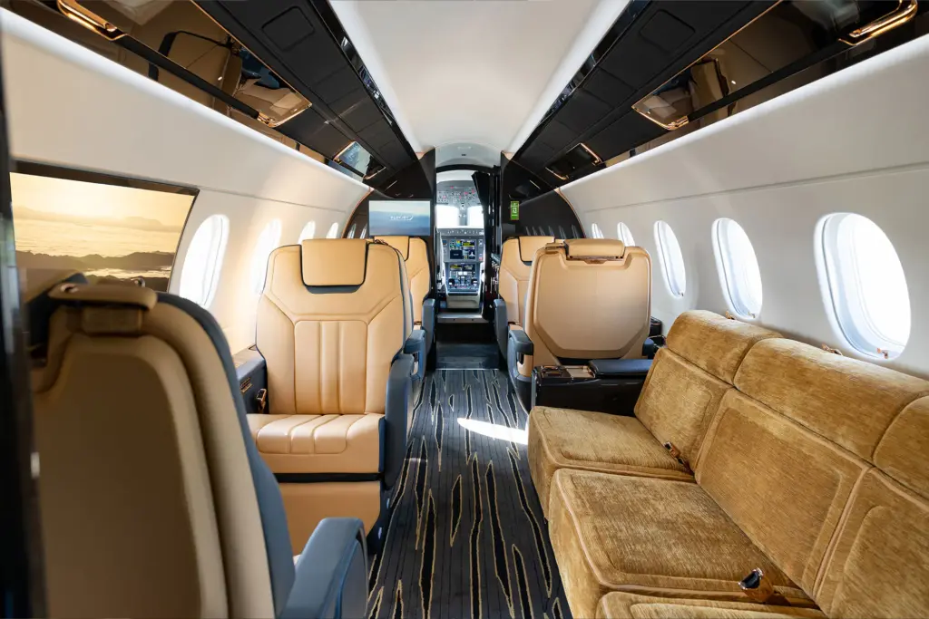 Interior cabin of an Embraer Praetor 600E business jet with tan leather seats and a sofa.