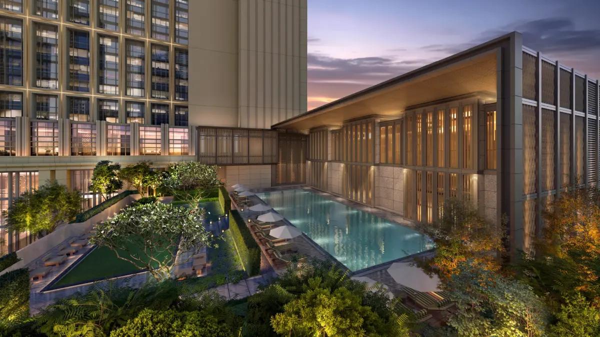 A rooftop swimming pool with loungers and lush landscaping between hotel buildings at dusk.