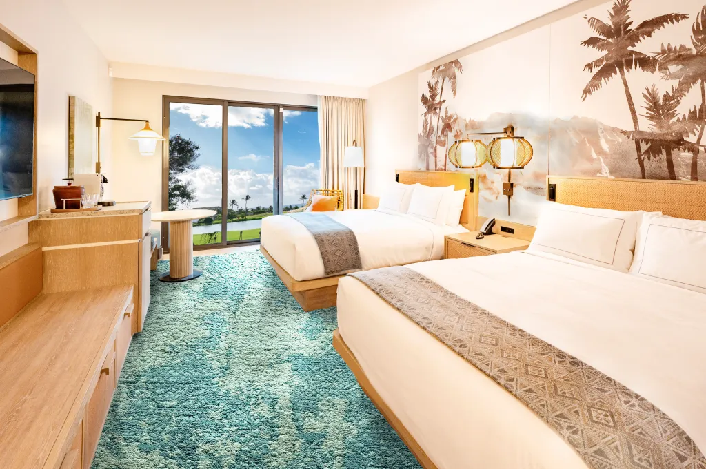 Hotel room with two beds, tropical palm tree wall art, teal carpet, and a balcony view of greenery and sky.
