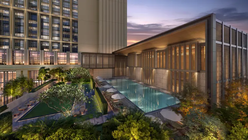 A rooftop swimming pool with loungers and lush landscaping between hotel buildings at dusk.