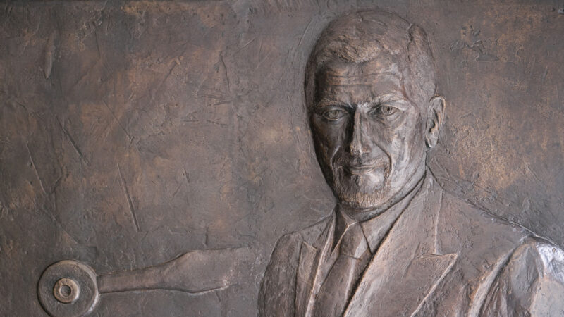 Bronze relief plaque depicting a man's portrait in a suit and tie.