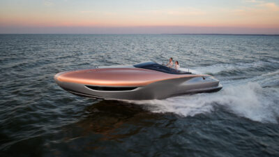 A copper and silver luxury motor yacht speeds across the water at dusk with two people aboard.