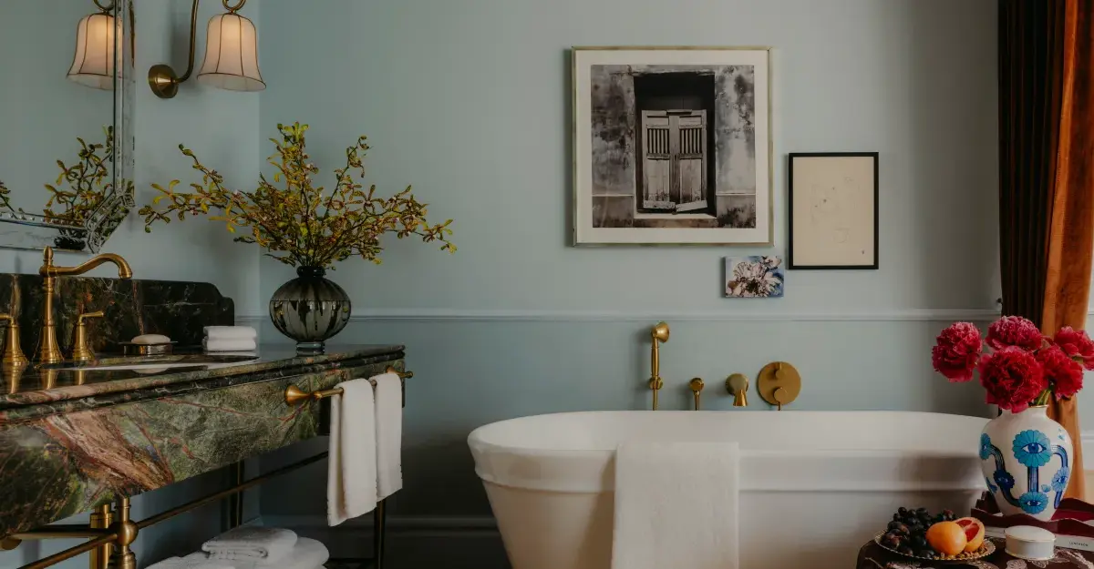 A luxury hotel bathroom with a marble vanity, freestanding tub, artwork, and floral arrangements.