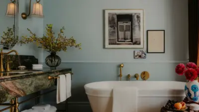 A luxury hotel bathroom with a marble vanity, freestanding tub, artwork, and floral arrangements.
