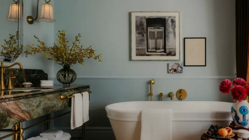 A luxury hotel bathroom with a marble vanity, freestanding tub, artwork, and floral arrangements.