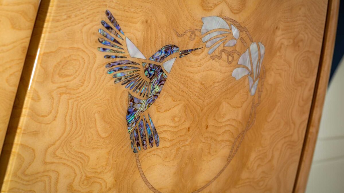Wood veneer panel with a hummingbird and flowers inlaid in abalone shell and mother-of-pearl.