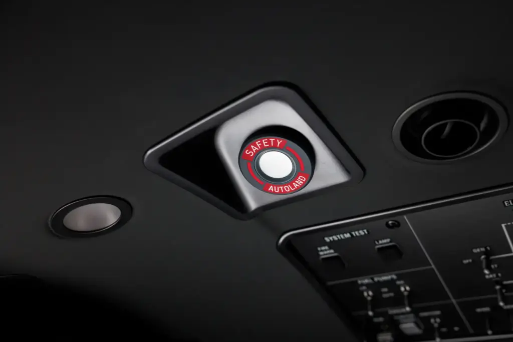 Close-up of the red and black 'Safety Autoland' button on an aircraft cockpit overhead panel.