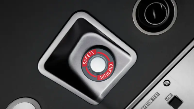 Close-up of a cockpit control panel with a red and grey button labeled Safety Autoland.