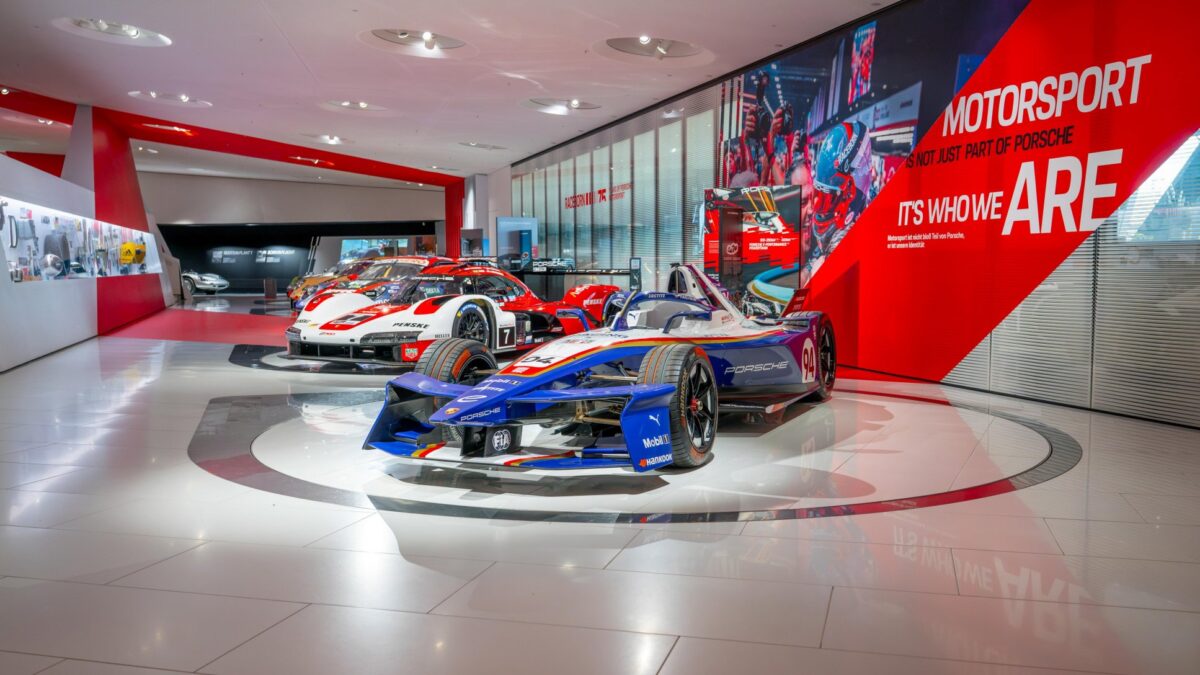 Porsche 99X Electric Formula E race car on display alongside other race cars in the Porsche Museum motorsport exhibition.