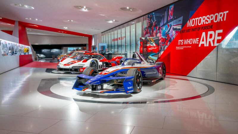 Porsche 99X Electric Formula E race car on display alongside other race cars in the Porsche Museum motorsport exhibition.