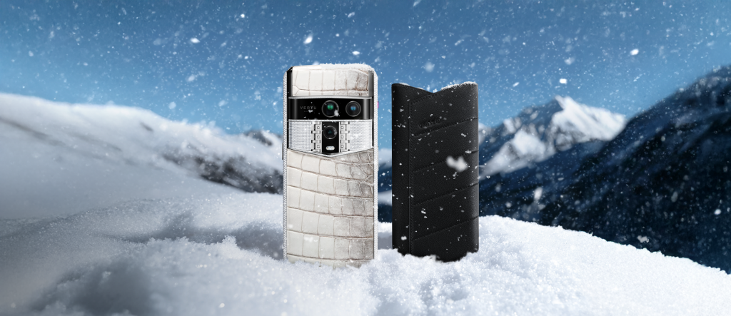 A Vertu smartphone with crocodile-textured back and a black leather case standing in snow against mountains.