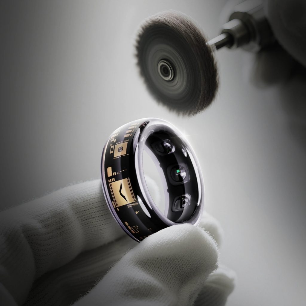 A gloved hand holds a smart ring with circuit patterns and sensor pads near a polishing wheel.