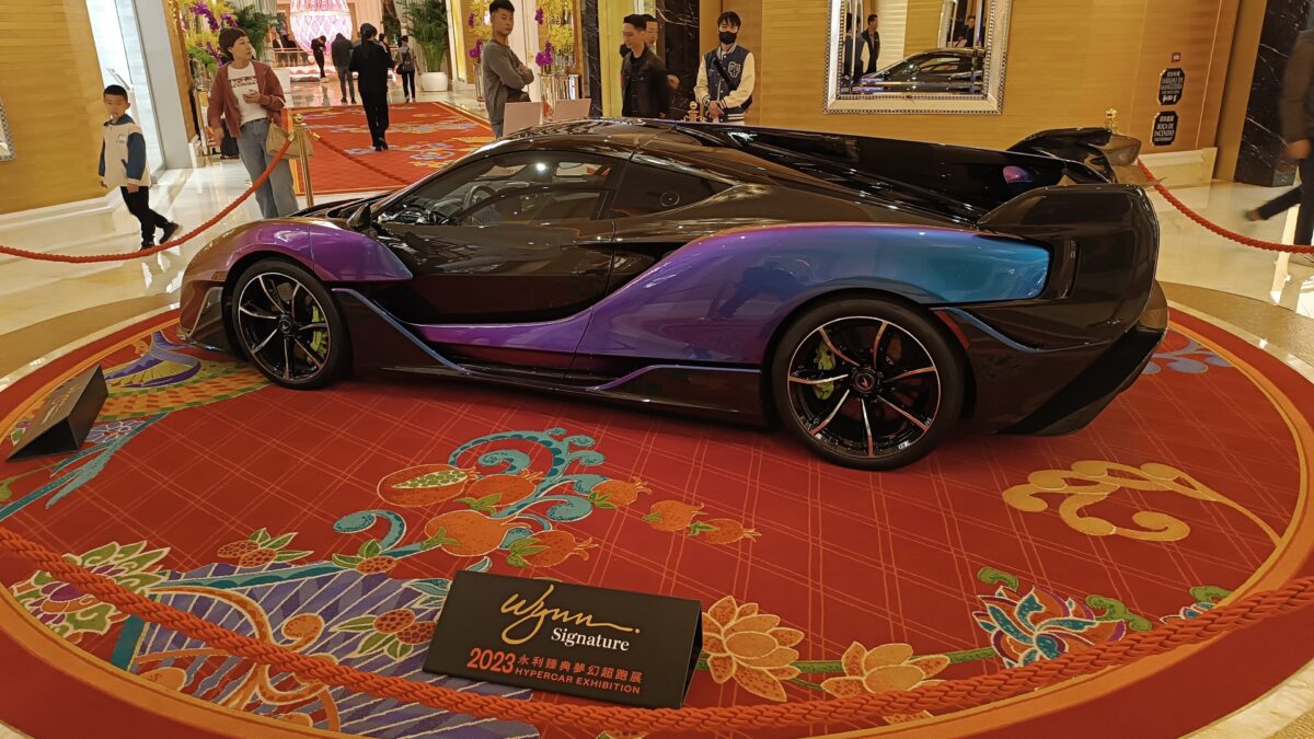 A purple and blue hypercar on display on a red carpet in the Wynn Palace lobby with a Wynn Signature exhibition sign.