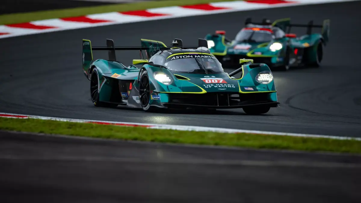 A teal Aston Martin Valkyrie race car numbered 007 leads two others on a racetrack.