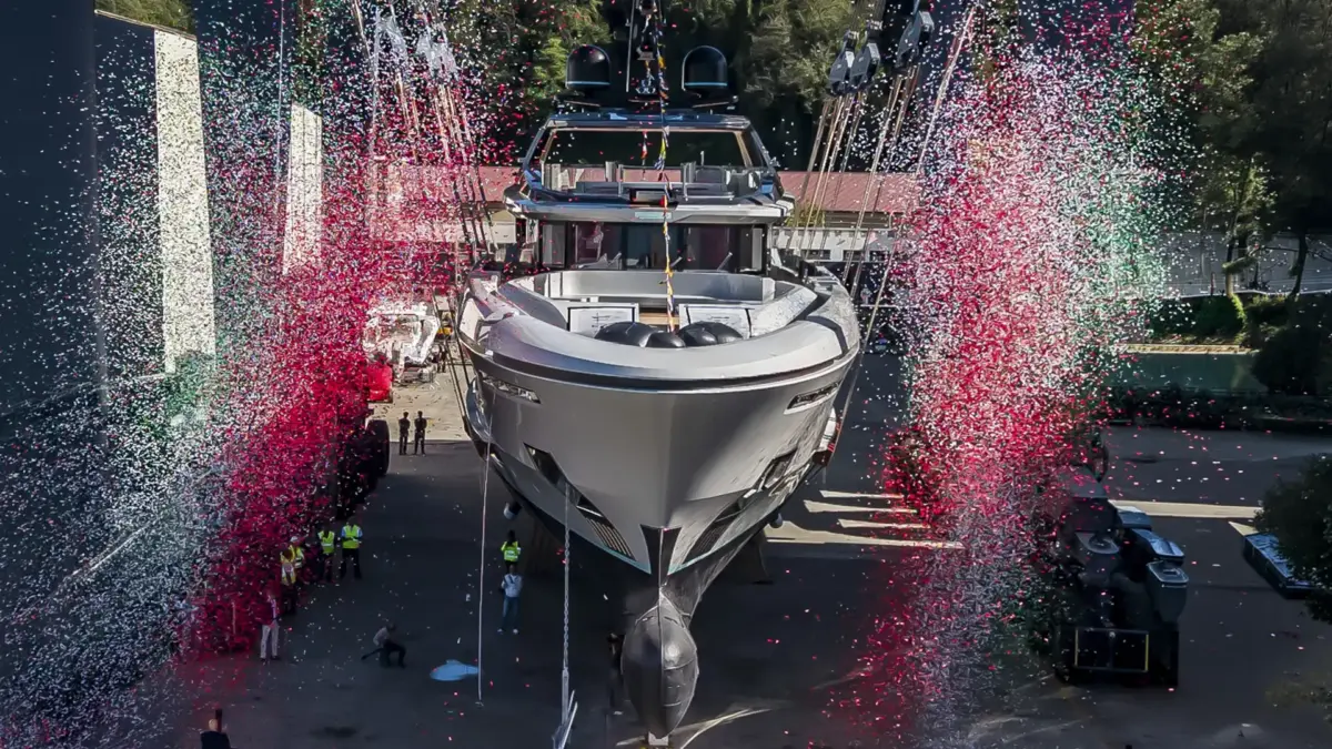 A superyacht sits on a launch cradle at a shipyard as red and white confetti rains down during a christening ceremony.