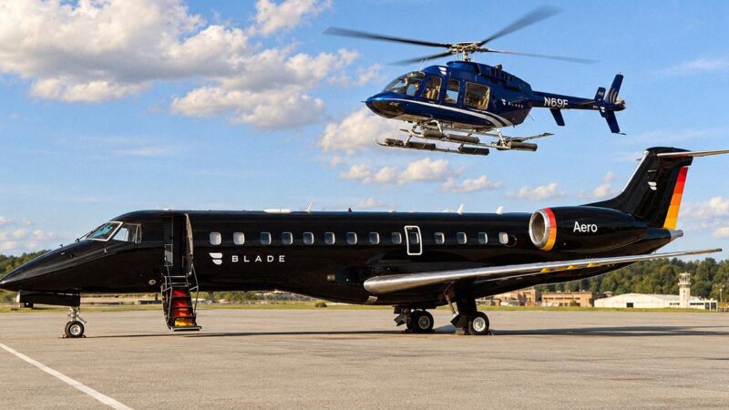 A black private jet marked BLADE and Aero sits on a tarmac as a blue BLADE helicopter flies above it.