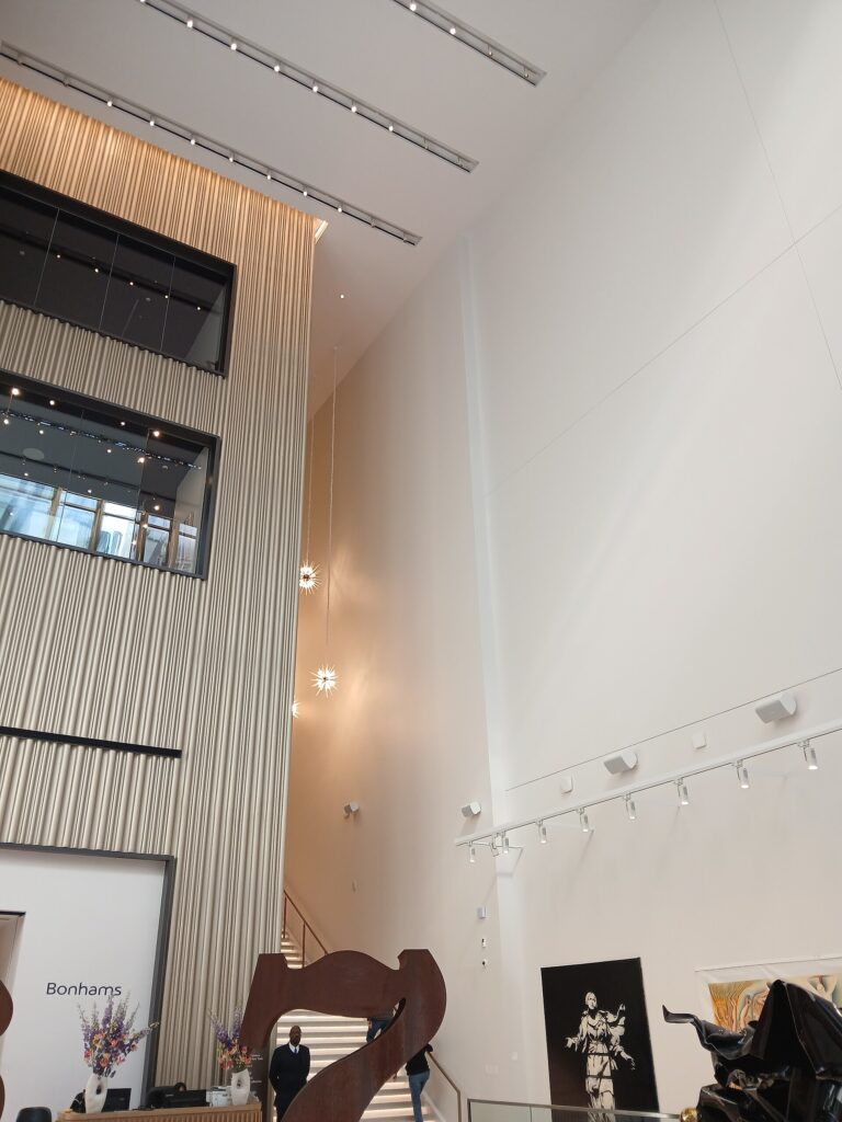 Interior of Bonhams auction house lobby with high ceilings, artworks, and a staircase, with the Bonhams sign visible.