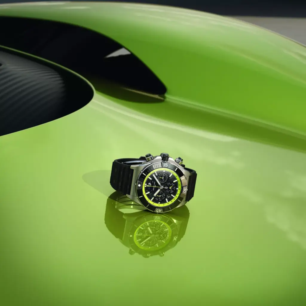 A Breitling chronograph watch with black and yellow dial resting on the lime green bodywork of an Aston Martin.