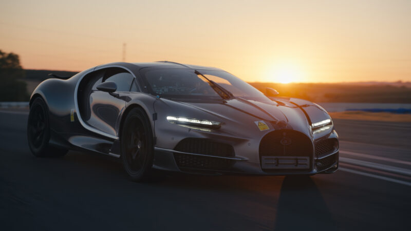 A gray Bugatti Tourbillon prototype car driving on a racetrack at sunset.