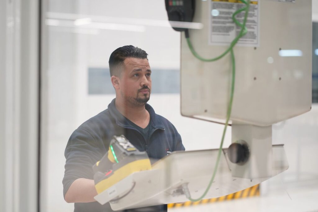 A man in a workshop uniform operates a control panel on industrial machinery.