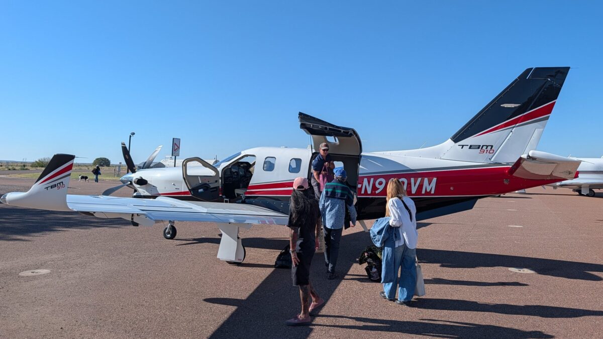 Passengers board a Daher TBM 910 turboprop aircraft parked on an airport tarmac.