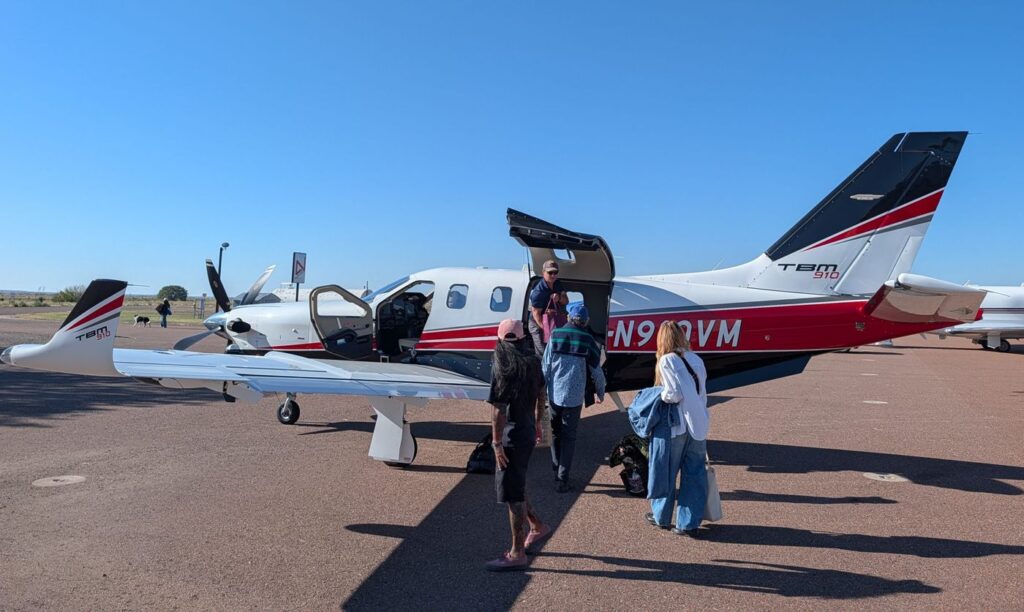 People boarding a Daher TBM 910 turboprop aircraft parked on an airport tarmac.