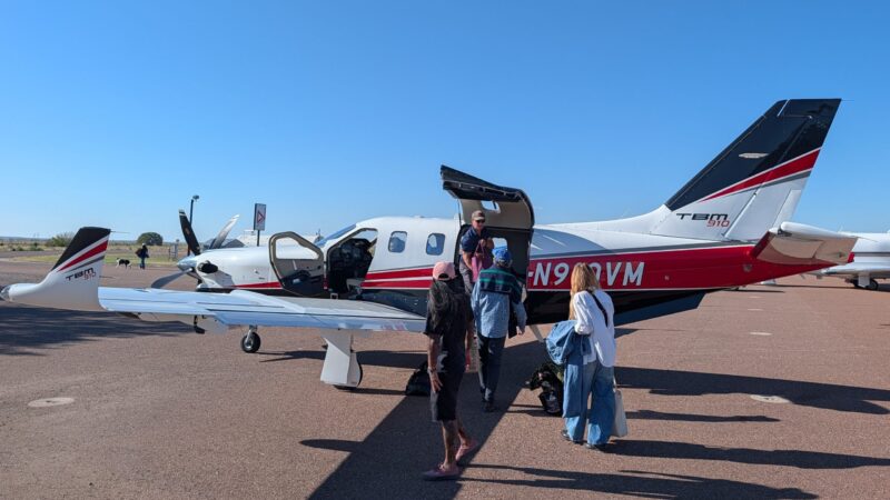 Passengers board a Daher TBM 910 turboprop aircraft parked on an airport tarmac.