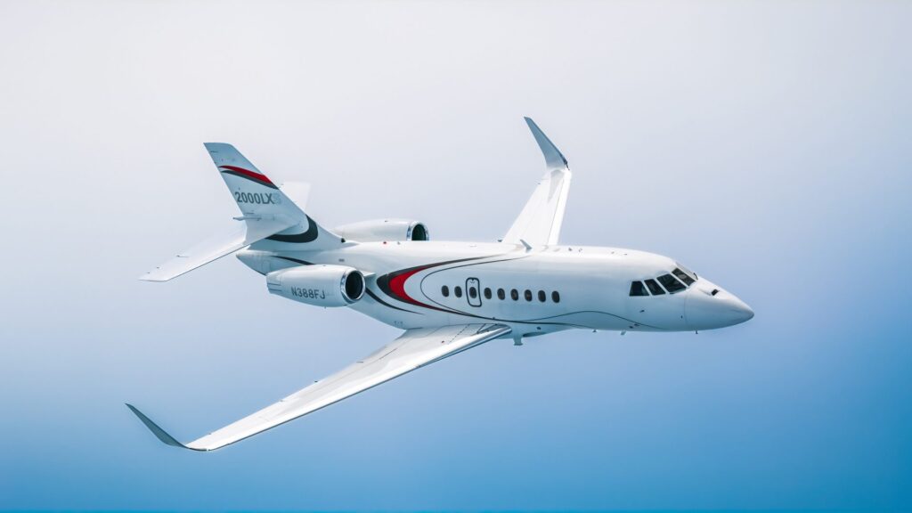 A white Dassault Falcon 2000LXS business jet banking in flight against a blue sky.