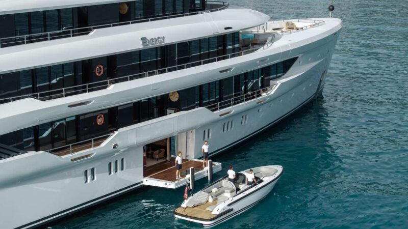 Aerial view of the superyacht ENERGY with crew on its swim platform and a tender boat docking alongside.