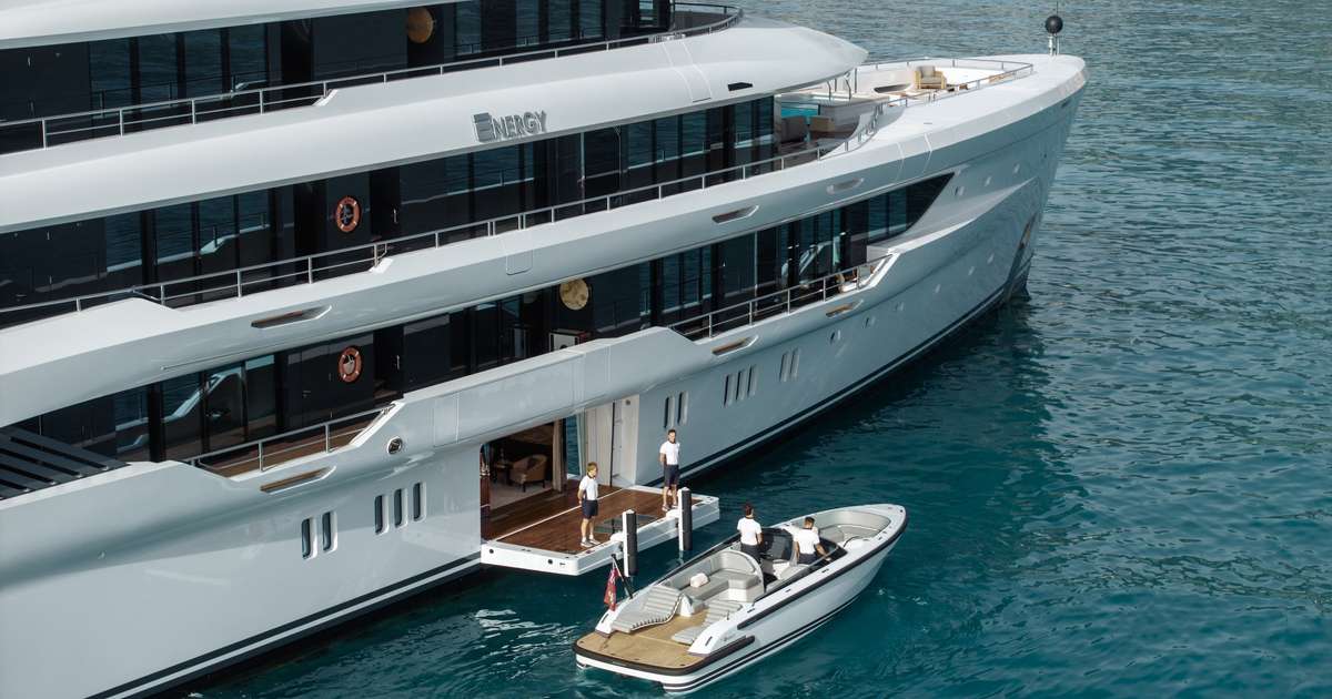 Aerial view of the superyacht ENERGY with crew on its swim platform and a tender boat docking alongside.