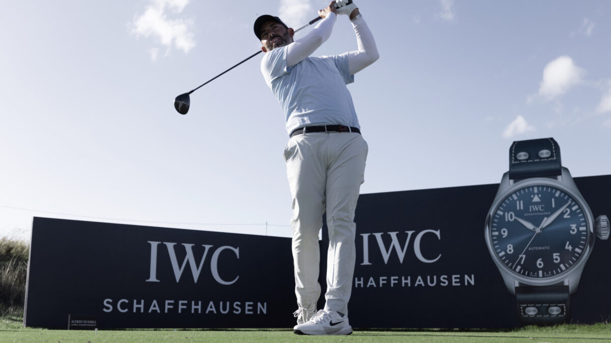 A golfer swings a club on a course in front of IWC Schaffhausen branded boards and a large watch graphic.