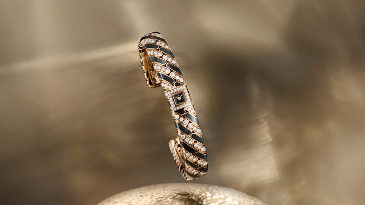 A gold bracelet watch with diamonds and black enamel chain-link design displayed vertically on a pedestal.