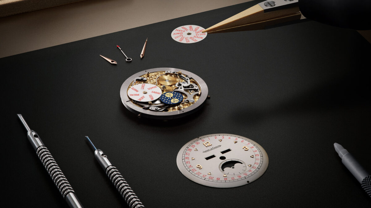 Jaeger-LeCoultre watch movement, calendar discs, and dial laid out on a workbench with tools.