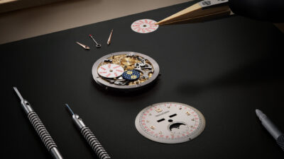 Jaeger-LeCoultre watch movement, calendar discs, and dial laid out on a workbench with tools.