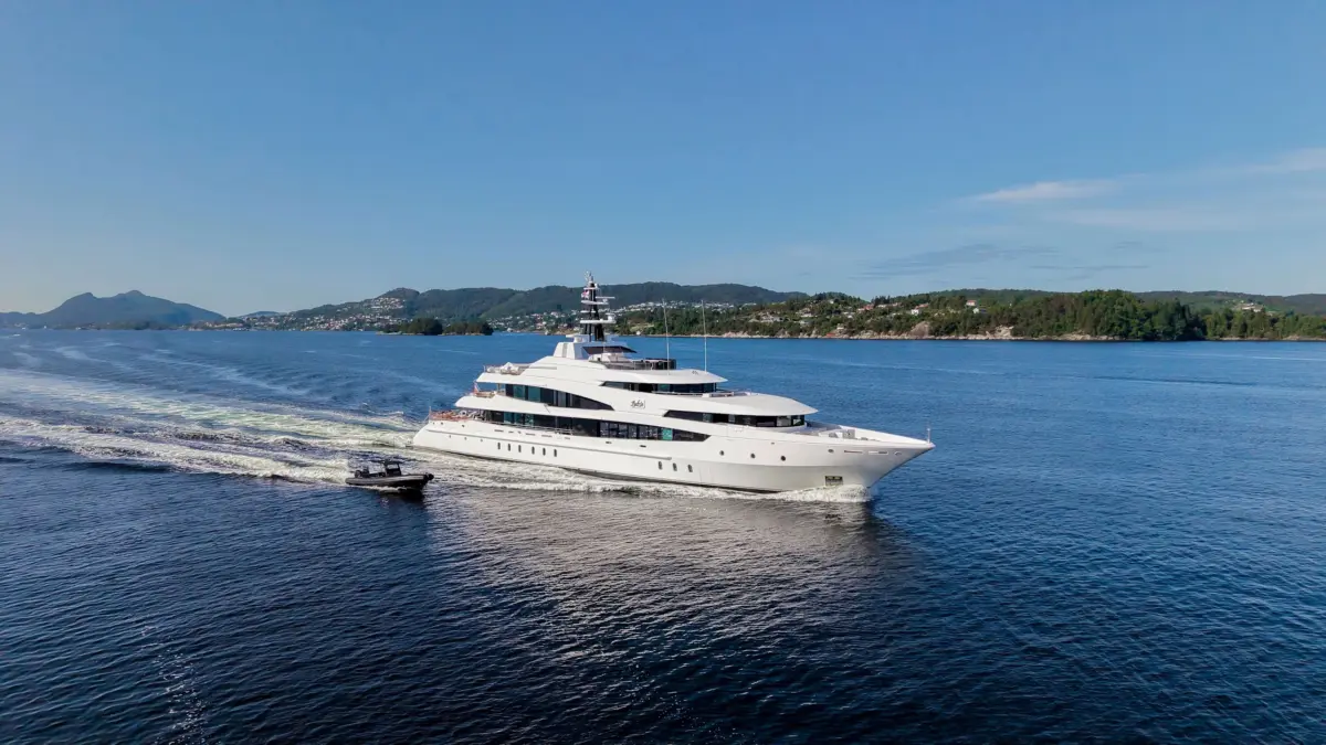 Aerial view of a large white motor yacht cruising near a green coastline with a small tender following.