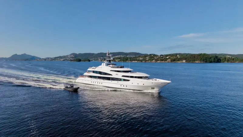 Aerial view of a large white motor yacht cruising near a green coastline with a small tender following.