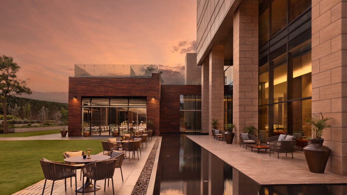 Hotel terrace with outdoor seating beside a reflecting pool and stone building facade at sunset.