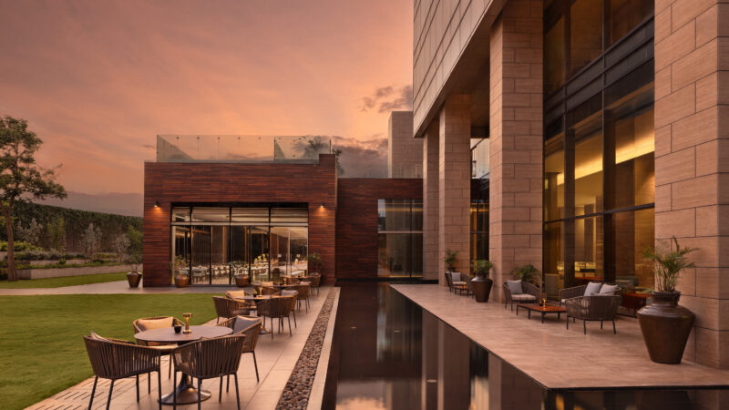 Hotel terrace with outdoor seating beside a reflecting pool and stone building facade at sunset.