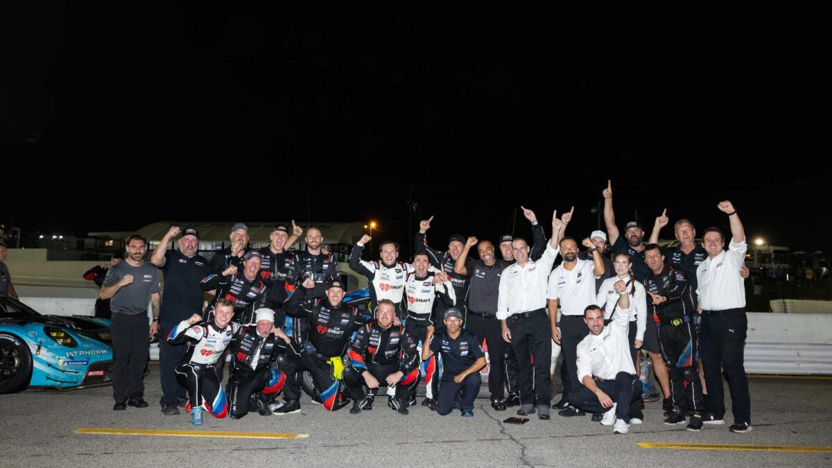 A racing team celebrates together on pit lane at night next to a BMW race car.