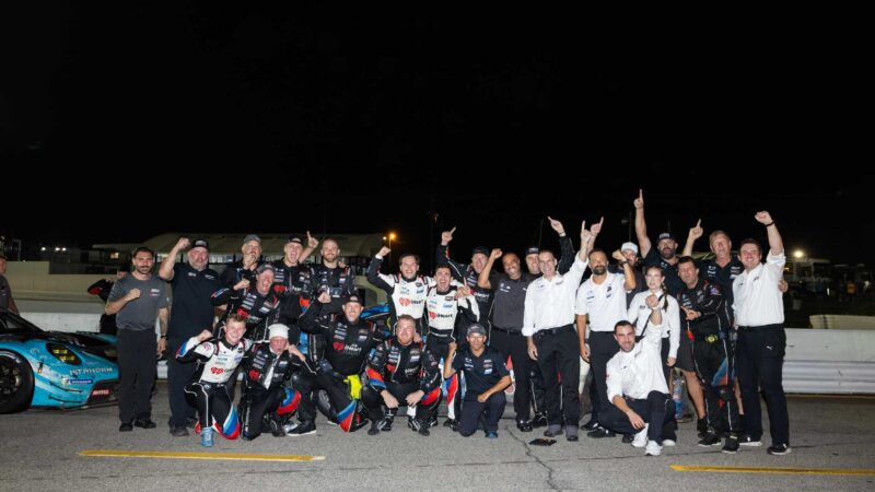 A racing team celebrates together on pit lane at night next to a BMW race car.