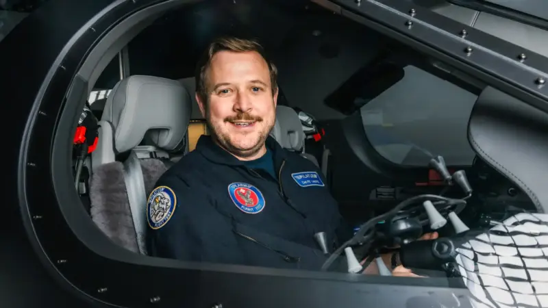 A man wearing a Pilatus flight test jumpsuit sits in the cockpit of a PC-12 PRO flight simulator.