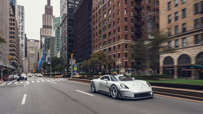 A white Porsche Mission S concept car drives down a city street in New York lined with tall buildings.