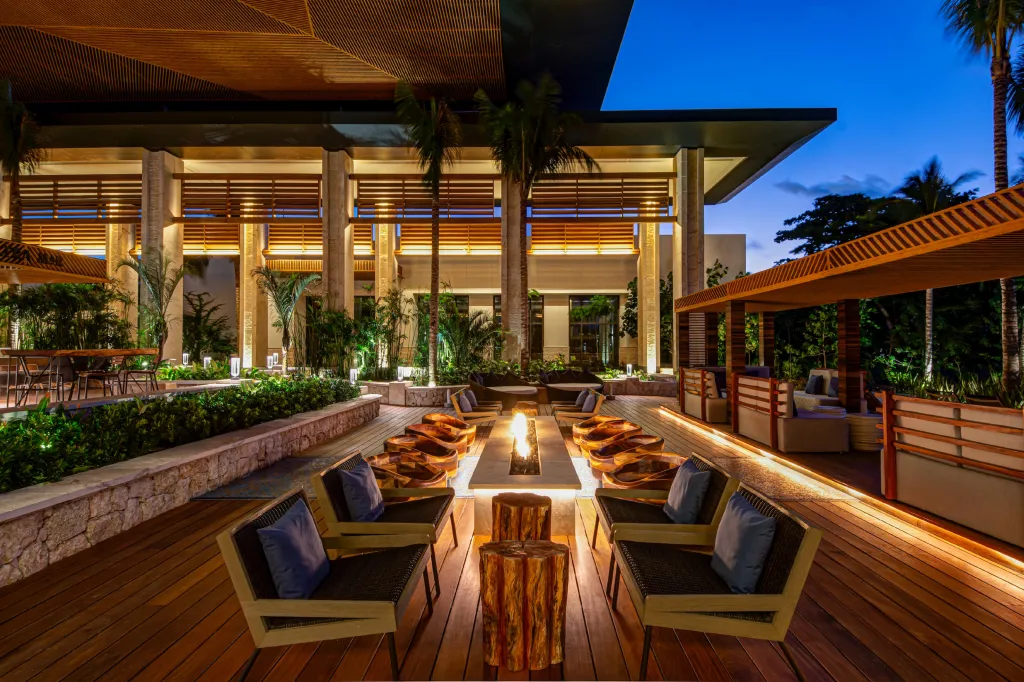 Outdoor lounge area with modern chairs around a fire pit on a wooden deck at a tropical resort at dusk.